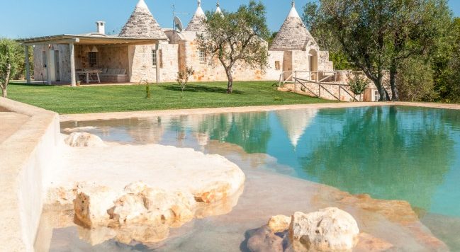 Ruhiges Trulli-Haus mit kristallklarem Pool, eingebettet in üppiges Grün und umgeben von malerischen Felsformationen.