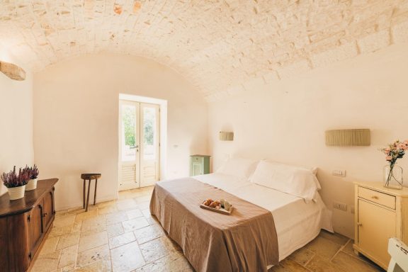 Luminous bedroom with a large bed, minimalist decor, and natural light from a door.