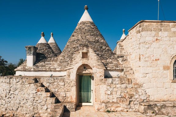 Trulli stone buildings with conical roofs against a clear blue sky.